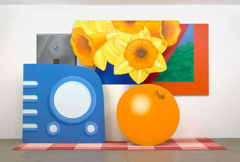 Tom Wesselmann. Still Life #57. 1969–70. Oil on canvas and base of acrylic paint on carpet, in six sections. Gift of the artist. © Tom Wesselmann/Licensed by VAGA, New York, NY Alt Text: A gallery installation view of five shaped paintings arranged as larger than life sized objects placed on a red checkered picnic blanket. On the left is a periwinkle blue radio, with four lighter blue buttons on the left side and a large circular speaker in the center with two small knobs below. Behind it is a silver metallic switch plate. In the back center is a blue and white vase holding a spray of yellow daffodils. To the right of the flowers is a red-framed window in the shape of an acute triangle, with an abstracted blue and green landscape. Below the window and flowers is an orange, with the navel facing up at the one o'clock position.