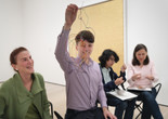 Photo: Martin Seck. © 2024 The Museum of Modern Art, NY Image Description: A smiling man wearing a purple button-up shirt holds up a sculpture of tangled colorful wires all tied together. His mother wearing a green cardigan smiles up at his artwork in the blurred background.