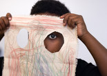 Photo: On White WallImage description: A child looks through a hole in their canvas drawing.