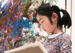Photo: Martin SeckImage description: A child looks at her own artwork while standing in front of a painting.