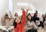 Photo: Martin SeckImage description: Children on the gallery floor hold their sheets of paper in the air.