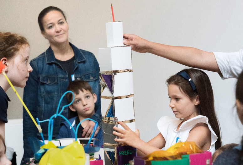 Photo: Martin SeckImage description: A child steadies a tower made out of cardboard while other workshop participants observe.