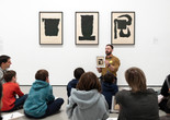 Photo: Martin SeckImage description: An educator holds up an image in front of three artworks while families observe.