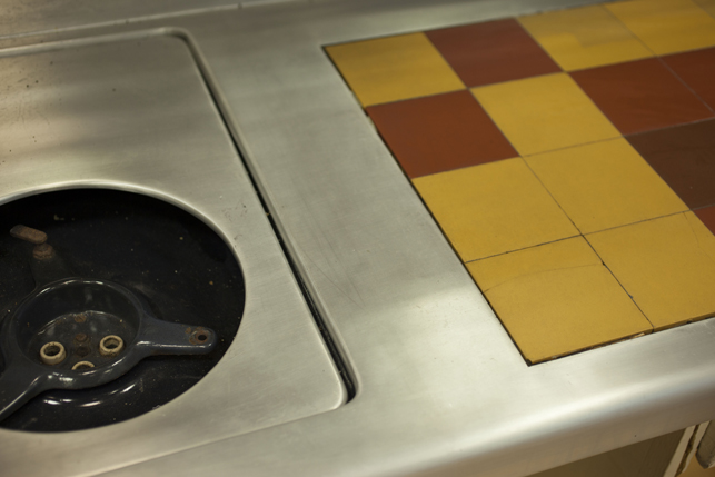 A detail of the bent and welded aluminum sheet countertop. The surface was polished to reduce the appearance of the welding lines. One can be seen running in-between the stove and the ceramic tiles. A detail of the bent and welded aluminum sheet countertop. The surface was polished to reduce the appearance of the welding lines. One can be seen running in-between the stove and the ceramic tiles.