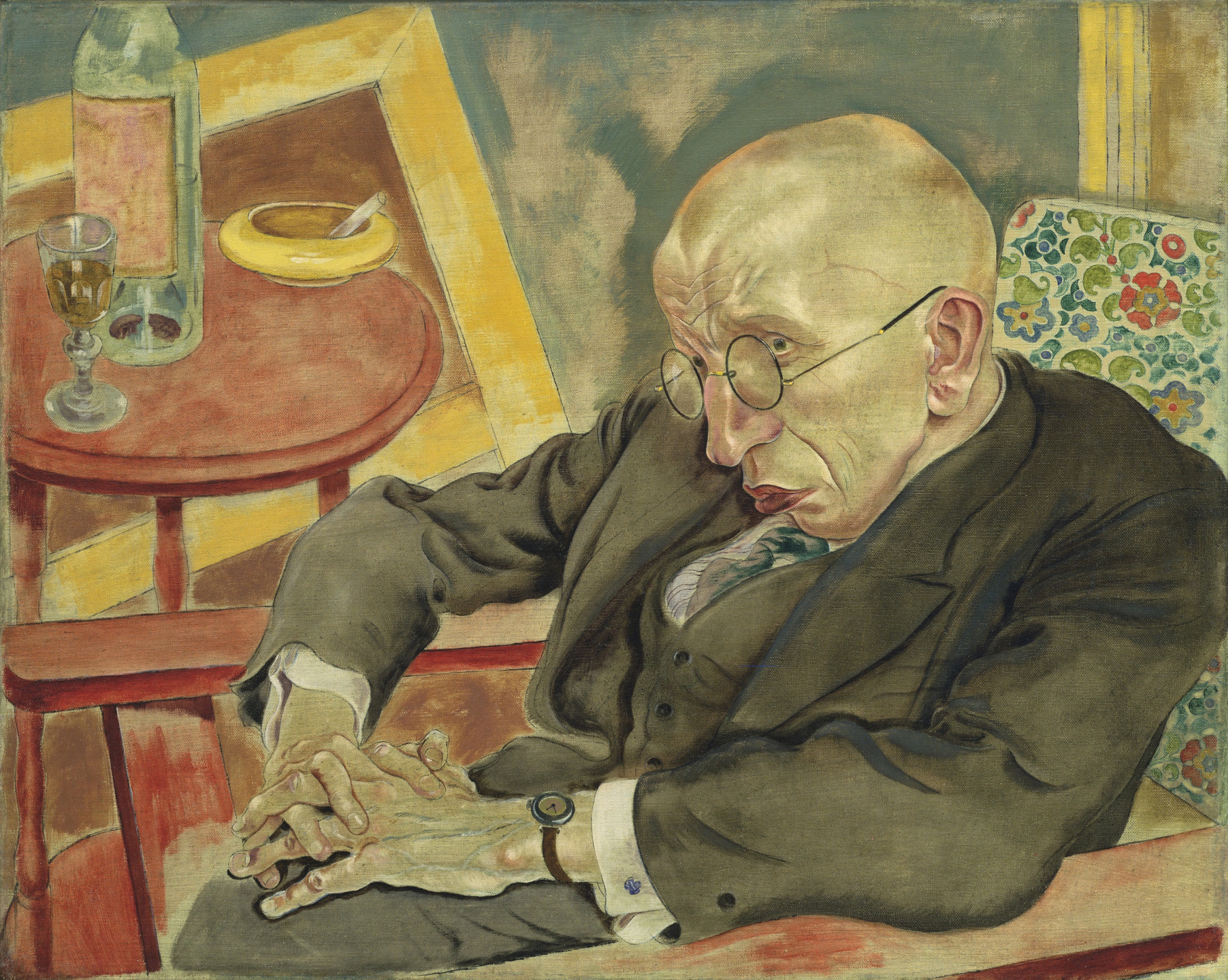 A person with round glasses, wearing a brown suit, sits in a chair with folded hands in their lap. A red table with a bottle, glass, and yellow ashtray is next to them. This is an AI generated description. To give feedback, email ai@moma.org.