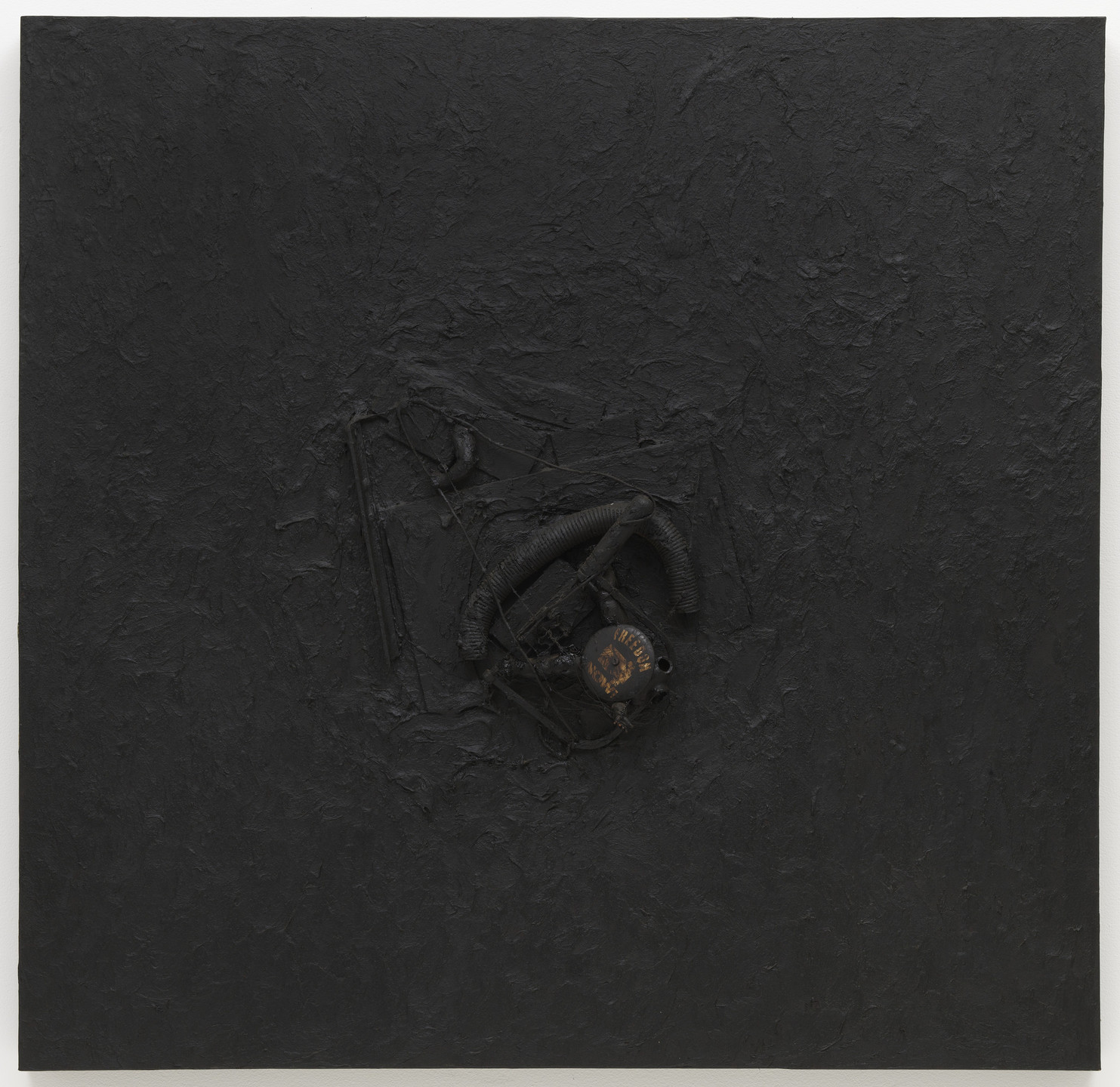 A textured black canvas displays a centrally embedded metal object with wires and tubes, partially covered by dark material. The predominant color is black. This is an AI generated description. To give feedback, email ai@moma.org.