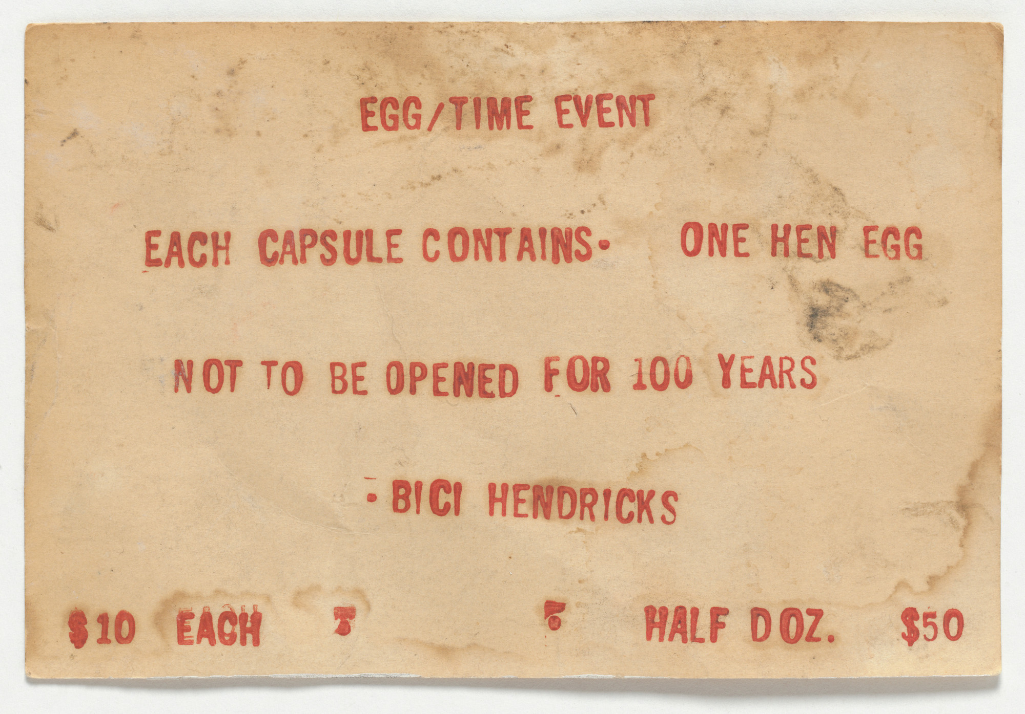 A weathered, beige paper with red text says, &#34;Egg/Time Event. Each capsule contains one hen egg. Not to be opened for 100 years.&#34; Pricing is &#34;$10 each, half doz. $50.&#34; This is an AI generated description. To give feedback, email ai@moma.org.