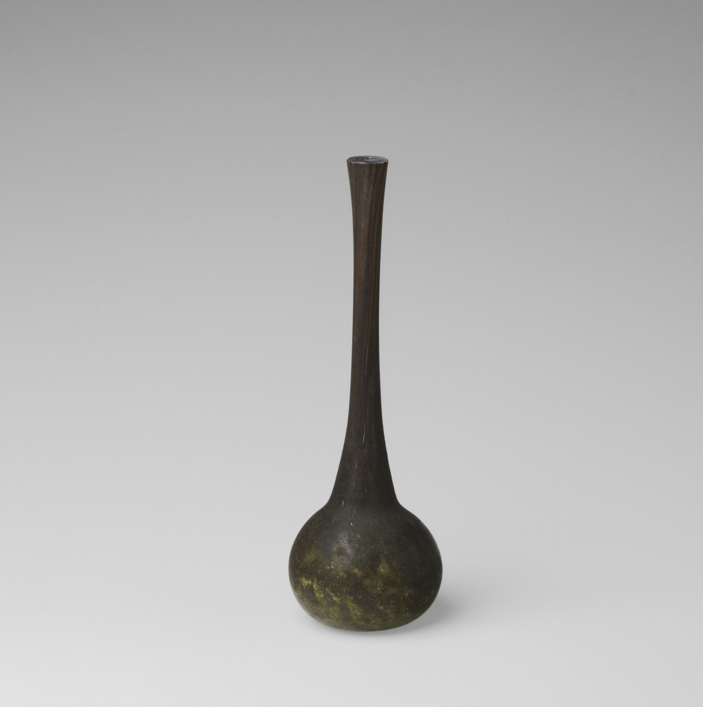 A dark, long-necked vase with a rounded base, predominantly black with specks of yellow-green, sits centered on a light gray background. The vase has a smooth, polished surface. This is an AI generated description. To give feedback, email ai@moma.org.