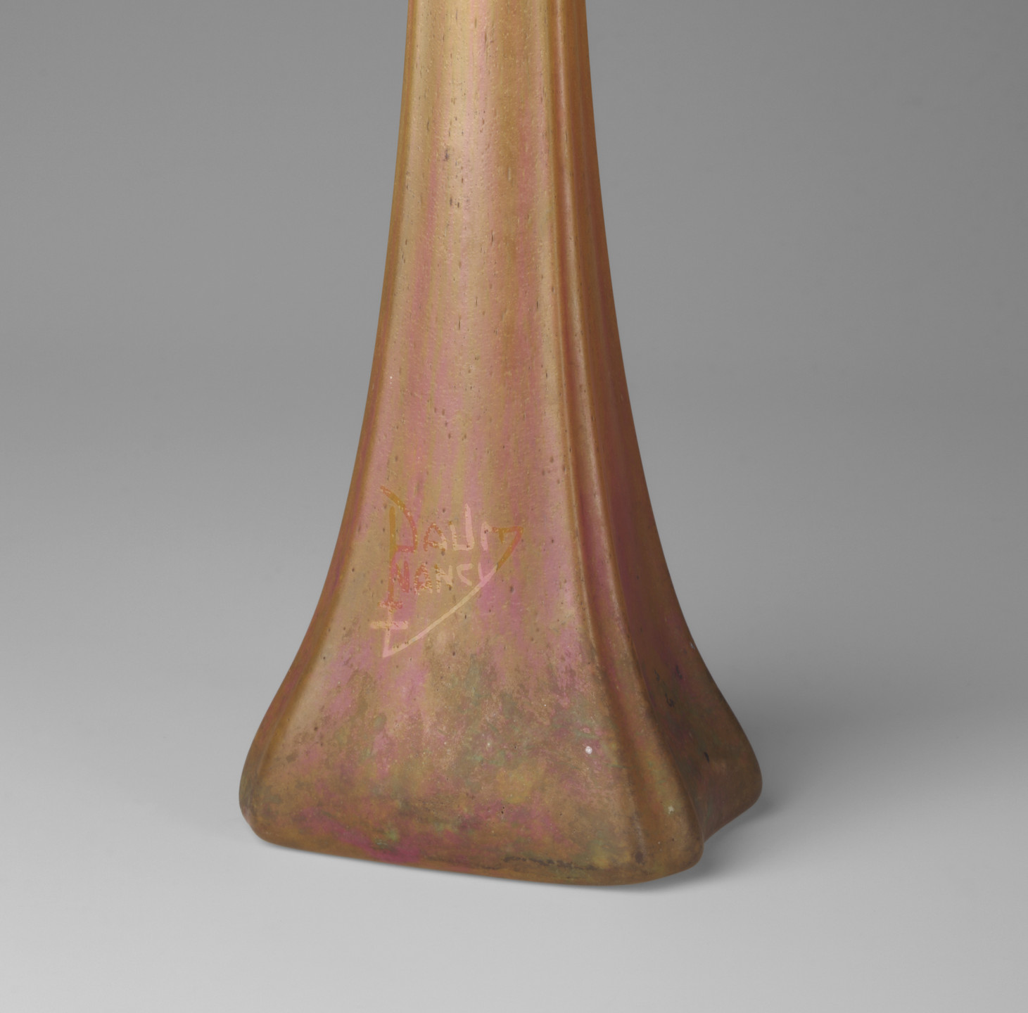 A tall, narrow vase with a square base, featuring a blend of gold and pink hues with an iridescent finish. The vase has a slightly aged appearance and shows a faint inscription near the base. This is an AI generated description. To give feedback, email ai@moma.org.