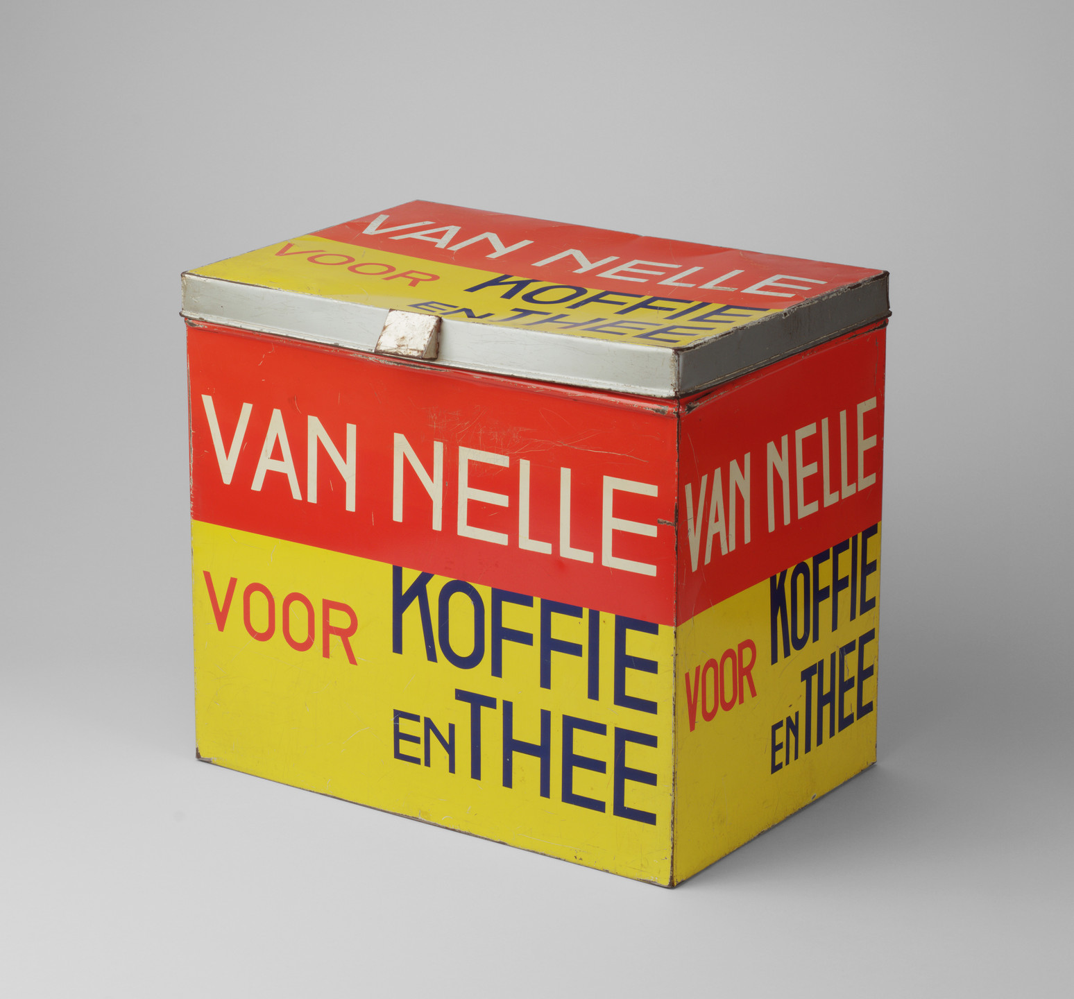 A rectangular metal box with a hinged lid, predominantly red and yellow, displaying text in white, red, and blue. The text includes &#34;VAN NELLE&#34; and &#34;VOOR KOFFIE EN THEE.&#34; This is an AI generated description. To give feedback, email ai@moma.org.