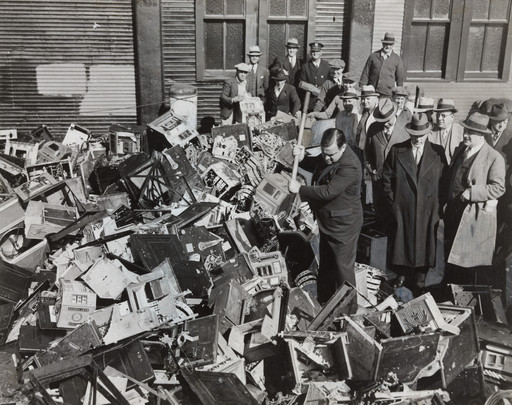 Times Wide World Photos. Mayor La Guardia Giving the Axe to Slot Machines Which Were Dumped in Waters off Scotland Light. October 13, 1934