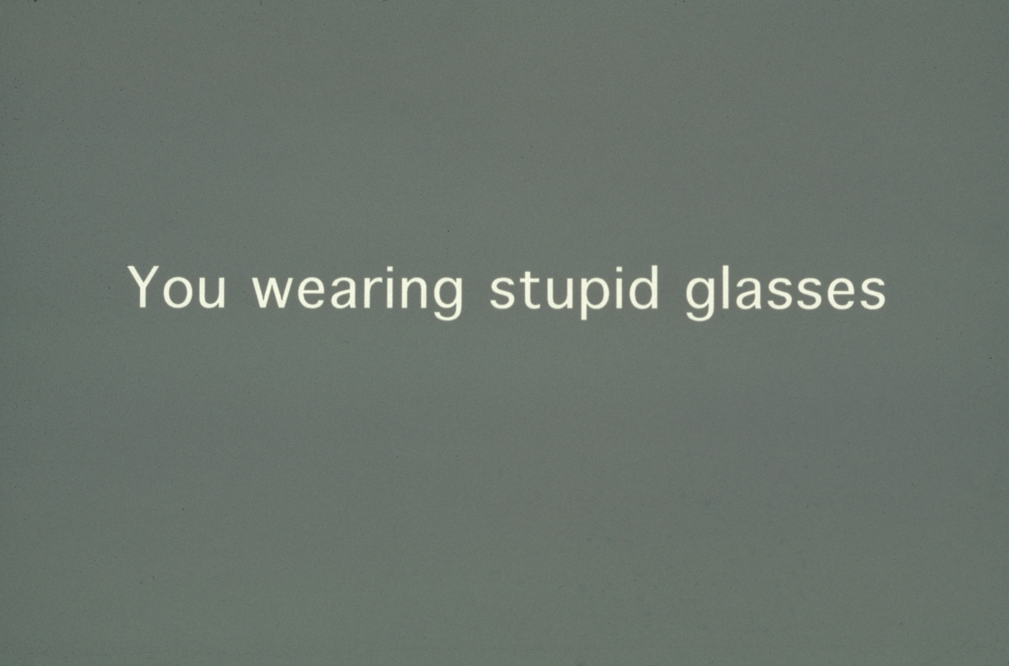 The image features light text on a muted green background stating, &#34;You wearing stupid glasses.&#34; The text is centered and in a simple white font. This is an AI generated description. To give feedback, email ai@moma.org.