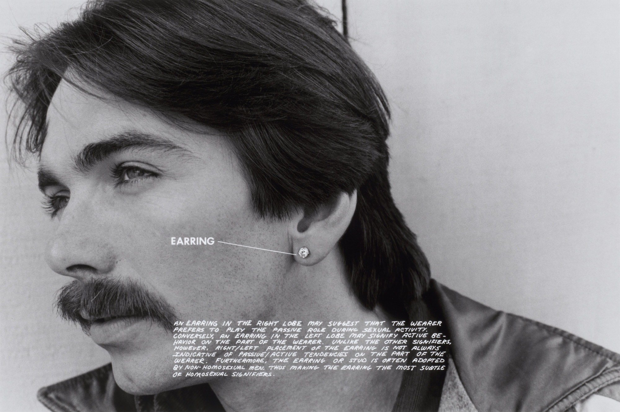 A black-and-white photo shows a close-up of a person's face with short, dark hair, a mustache, and a stud earring in their right ear. Text on the image labels the "EARRING" and provides comments on its implications. This is an AI generated description. To give feedback, email ai@moma.org.