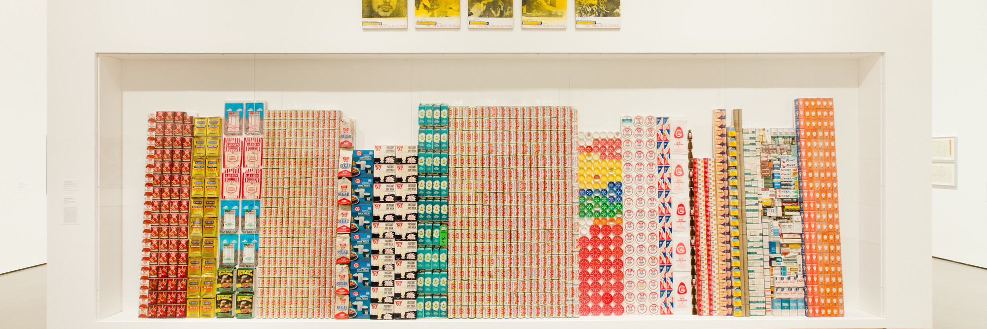 George Maciunas. One Year. 1973–74. Various empty containers and packaging. Above: Alison Knowles. Selections from The Identical Lunch. 1969. Screenprints on canvas. Installation view of both works at MoMA. The Museum of Modern Art, New York. The Gilbert and Lila Silverman Fluxus Collection. Photo: Jason Mandella