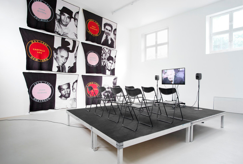 James Richards. Foreground: Active Negative programme. 2008. Video (color, sound). 20 min. Background: Untitled Merchandise (Lovers & Dealers). 2012. Six machine-knitted nylon blankets. 152 x 228 cm. Installation view from The Imaginary Museum, Kunstverein Munich, 2012. Courtesy the artist and Rodeo, Istanbul and London and Cabinet, London