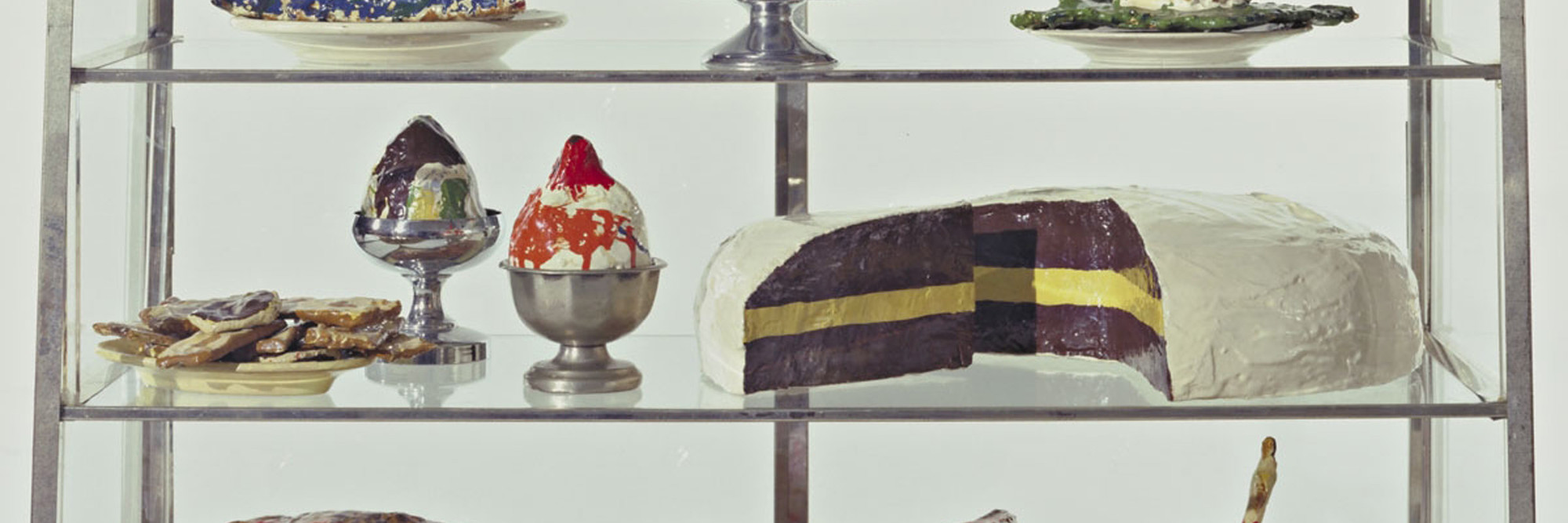 Claes Oldenburg. Pastry Case, I. 1961–62. Painted plaster sculptures on ceramic plates, metal platter, and cups in glass-and-metal case, 20 3/4 × 30 1/8 × 14 3/4″ (52.7 × 76.5 × 37.3 cm). The Museum of Modern Art, New York. The Sidney and Harriet Janis Collection. © 2012 Claes Oldenburg