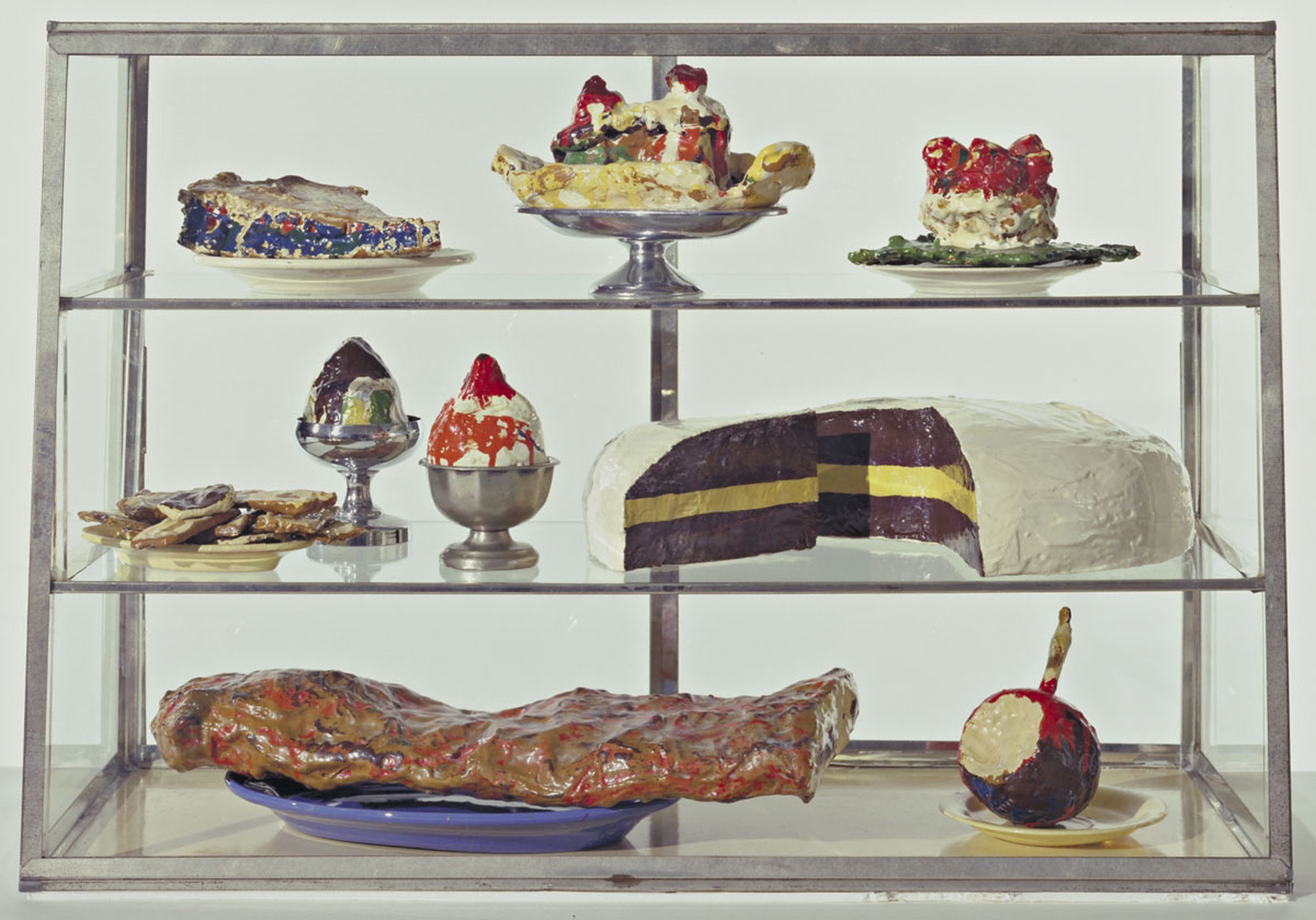 Painted plaster sculptures on ceramic plates, metal platter and cubs in glass-and-metal case. 20 3/4 x 30 1/8 x 14 3/4” (52.7 x 76.5 x 37.3 cm). The Museum of Modern Art, New York. The Sidney and Harriet Janis Collection. © 1961–62 Claes Oldenburg. Photo: MoMA Imaging Services