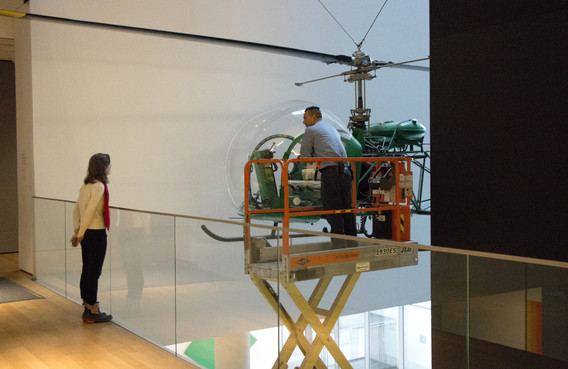 Artist Nina Katchadourian watches the dusting of the helicopter. Shown: Arthur Young. Bell-47D1 Helicopter. 1945. Manufacturer: Bell Helicopter Inc., Buffalo, NY. Aluminum, steel, and acrylic plastic, 9′ 2 3/4″ × 7′ 11″ × 42′ 8 3/4″ (281.3 × 302 × 1271.9 cm). Marshall Cogan Purchase Fund. Photo: Manuel Martagon. © 2016 The Museum of Modern Art