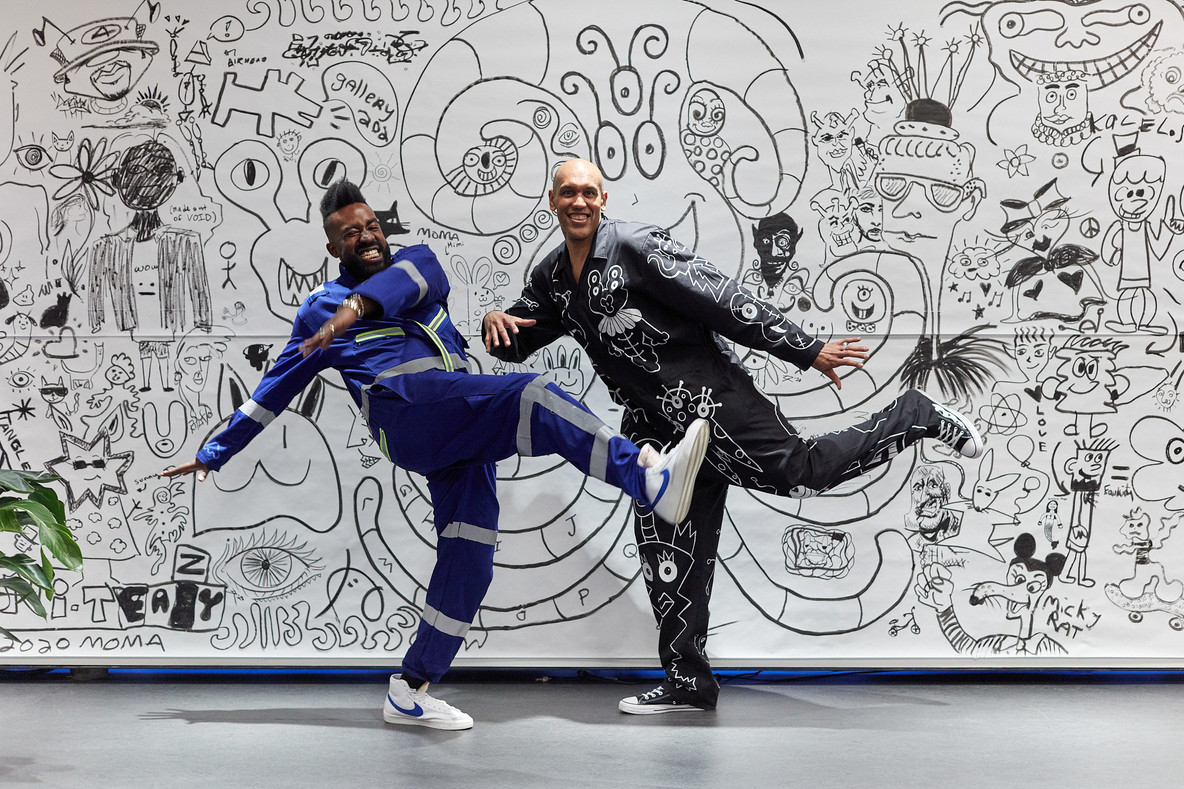 Chet Gold and Brian Wilson pose in front of a collective mural made with visitors and inspired by Keith Haring