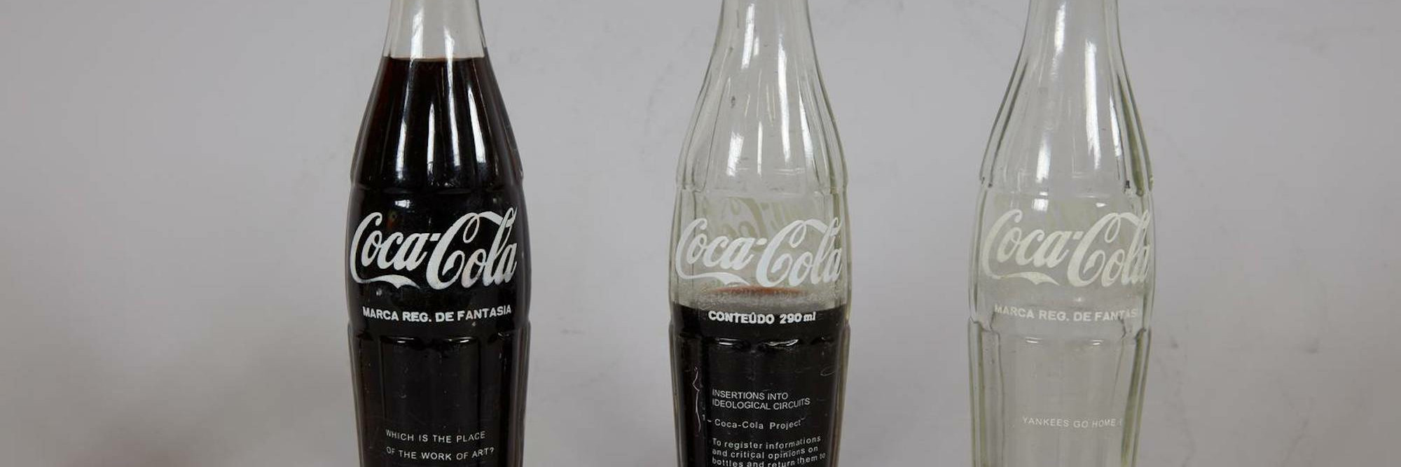 Cildo Meireles. INSERTIONS INTO IDEOLOGICAL CIRCUITS: 1. COCA-COLA PROJECT (INSERÇÕES EM CIRCUITOS IDEOLÓGICOS: 1. PROJETO COCA-COLA). 1970. Printed pressure-sensitive labels on three commercial glass bottles, dimensions variable. Gift of Lilian Tone.