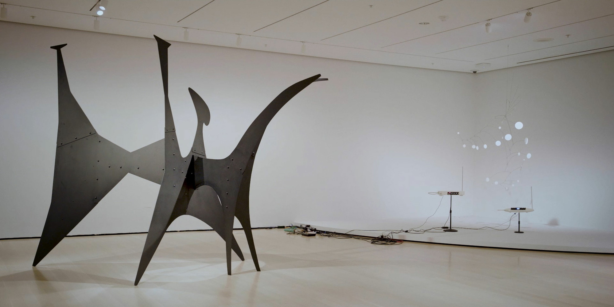 A still from the Calder Plays Theremin video. Shown, from left: Alexander Calder. Black Beast. 1940. Sheet metal, bolts, and paint. Calder Foundation, New York. © 2021 Calder Foundation, New York/Artists Rights Society (ARS), New York; Alexander Calder. Snow Flurry, I. 1948. Painted sheet steel and steel wire. The Museum of Modern Art, New York. Gift of the artist. © 2021 Calder Foundation, New York/Artists Rights Society (ARS), New York