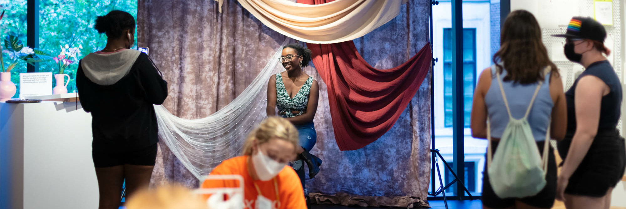 Photo of a person smiling and posing for a picture in front of a brown, red, and white photo backdrop in the Creativity Lab. The Museum of Modern Art, New York. Digital Image ©️ 2022 The Museum of Modern Art, New York. Photo: Beatriz Meseguer/onwhitewalls.com
