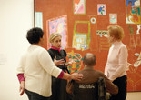 A photograph of an educator in conversation with three adults in front of the large-scale painting The Red Studio by the artist Henri Matisse. Photo: Jason Brownrigg. Digital Image © 2022 The Museum of Modern Art, New York