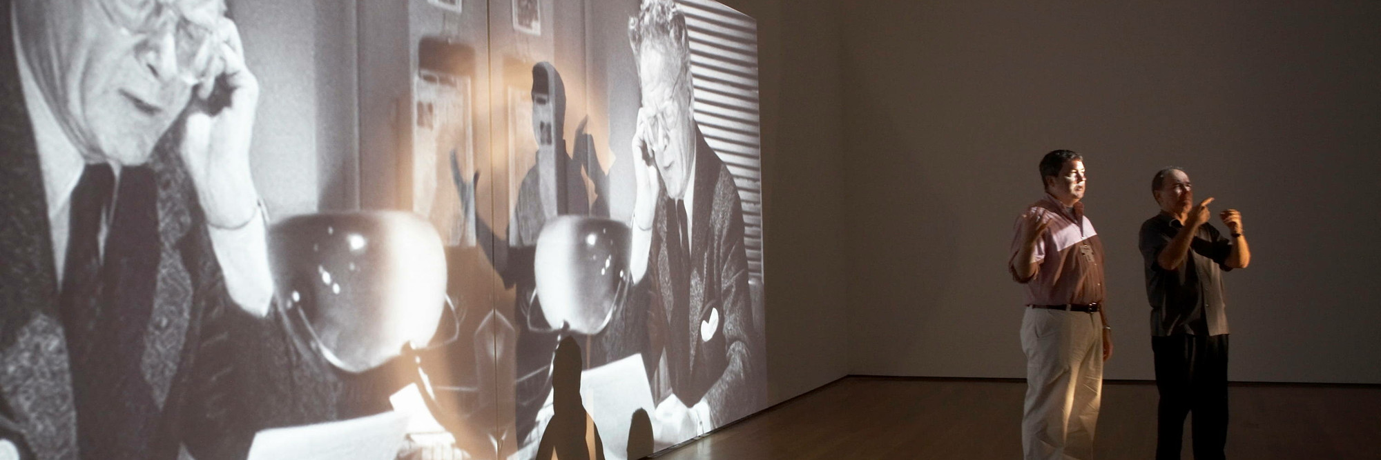 The Museum of Modern Art, New York. Photo: Robin Holland Image Description: A photograph of a lecturer and sign language interpreter standing in front of a black and white film projected onto the gallery wall.