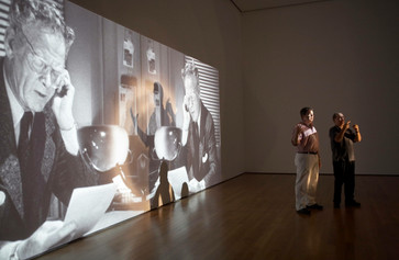 The Museum of Modern Art, New York. Photo: Robin Holland Image Description: A photograph of a lecturer and sign language interpreter standing in front of a black and white film projected onto the gallery wall.