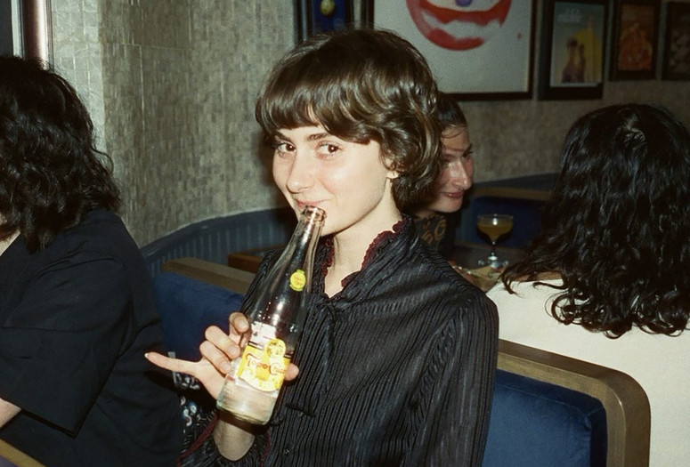 Portrait of Aimee France. Photo: Parker Hao. Courtesy of the Artist Image Description: Artist and Baker Aimee France sits in a restaurant booth holding a seltzer while smiling at the camera.