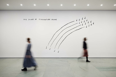Installation view, Christine Sun Kim. The Sound of Temperature Rising. 2019. Screenprint on wall, dimensions variable. Fund for the Twenty-First Century. ©️ Christine Sun Kim Image description: A horizontally oriented photograph shows a black screenprinted artwork on a white gallery wall with two blurry museum visitors walking by. On the wall, four black lines arc upwards from left to right in the shape of a half rainbow. A musical note is at the base of each line and four musical notes are at the top of each line. The words “The Sound of Temperature Rising” are printed in black across the top of the wall.