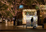 Man Push Cart. 2005. USA. Directed by Ramin Bahrani Image description: A photograph of a man standing inside his street food cart on a New York City sidewalk at night. The street is lined with twinkle light–wrapped trees, and cars and people pass by.