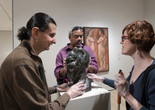 A horizontally oriented photograph of three museum visitors touching a bumpy bronze bust by artist Pablo Picasso on a white pedestal in a gallery. They wear plastic gloves and discuss the sculpture. Photo: Martin Seck. ©️ 2023 The Museum of Modern Art, New York