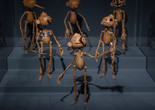 Installation view of Guillermo del Toro: Crafting Pinocchio, The Museum of Modern Art, New York, December 11, 2022–April 15, 2023. Photo: Emile Askey Image description: An exhibition installation photograph of six wooden Pinocchio puppets with various carved facial expressions standing in three rows on a step platform, with a dark blue background. The center puppet has a smile and a long pointed nose, with one arm up gesturing in the air.