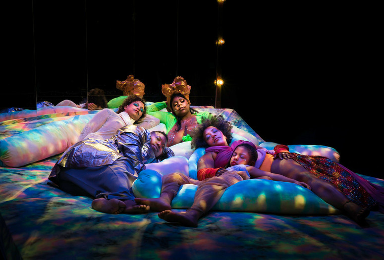 Black Power Naps installation at Performance Space, 2019. Courtesy of Black Power Naps. Photo: Avi Avion Image description: Four adults and one child sleep on colorfully dyed cushions under soft, dappled lighting.