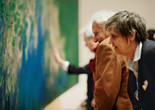 Photo: Jason Brownrigg ©️ 2024 The Museum of Modern Art, NY. Image description: Side view of a group of adults looking closely at a blue and green abstract painting that fills the wall.