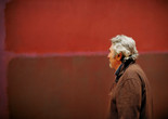 Photo: Jason Brownrigg ©️ 2024 The Museum of Modern Art, NY. Image description: Profile of a man with grey hair, a brown jacket, and reading glasses hung around his neck looking at a Rothko artwork with two red shaded squares on a lighter red background.