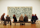 Photo: Jason Brownrigg ©️ 2024 The Museum of Modern Art, NY. Image description: Eight adults seated, facing Jackson Pollock’s One: Number 31, a wall-filling beige canvas scattered with dark gray, white, blue, and tan drips that erratically swing in abstract movement.