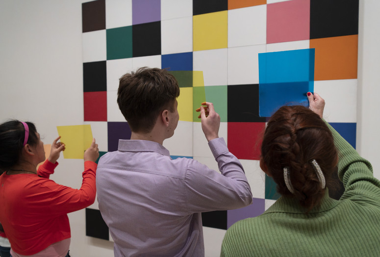 Photo: Martin Seck. © 2023 The Museum of Modern Art, New York Image description: Three people hold up sheer, colorful plastic squares to look at an artwork on the wall with a grid of black, white, and colorful painted squares by the artist Ellsworth Kelly.