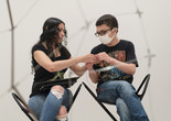 Photo: Martin Seck. © 2024 The Museum of Modern Art, NY Image Description: A woman with long curly hair and a tangle of colorful wires in her lap folds a red wire with her son, a teenage boy wearing a white facemask, sitting next to her in gallery stools.