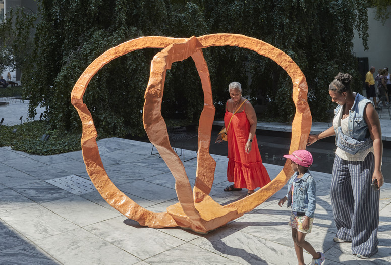 Photo: Franz West. Untitled (Orange). 2006. Polyester. The Museum of Modern Art, New York. Scott Burton Fund. © 2023 Estate of Franz West. Photo: Gus Powell Image description: A family in the Sculpture Garden observes the work titled Untitled (Orange) by Franz West.