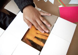 Photo: Martin Seck Image description: A child&#39;s hand with brown skin is holding a cardboard rectangle with a transparent orange square in the center. The child&#39;s other hand can be seen, face up, pressed against the underside of the orange square.