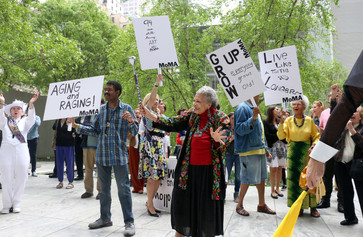 Photo: Manuel Molina Martagon. ©️ 2023 The Museum of Modern Art, New York Image description: A group of older adults are gathered outside in MoMA’s Sculpture Garden with a marching band. The crowd wears colorful clothing and hold signs that read, “Aging and Raging!” and “Grow Up! Everyone Grows Old!”
