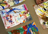 Image courtesy Tara Ridgedell Image description: A hand reaches toward four colorful prints made up of shapes, lines, and words.