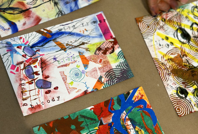 Image courtesy Tara Ridgedell Image description: A hand reaches toward four colorful prints made up of shapes, lines, and words.