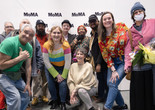 The Community Access Art Collective artists at their exhibition opening. Photo: Beatriz Meseuger/onwhitewall.com. ©️ 2024 The Museum of Modern Art, New York Image description: The Community Access Art Collective artists celebrate at their exhibition opening. Eleven colorfully dressed artists and studio staff pose in front of a backdrop with the MoMA logo printed in black and white. A person in the center holds a paper sign with the words &#34;Thank You&#34; written in blue ink, and two other people hold bouquets of flowers.