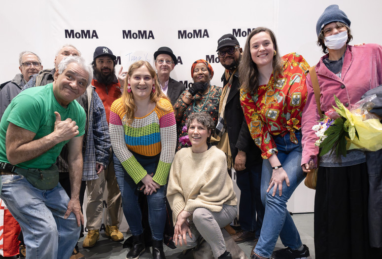 The Community Access Art Collective artists at their exhibition opening. Photo: Beatriz Meseuger/onwhitewall.com. ©️ 2024 The Museum of Modern Art, New York Image description: The Community Access Art Collective artists celebrate at their exhibition opening. Eleven colorfully dressed artists and studio staff pose in front of a backdrop with the MoMA logo printed in black and white. A person in the center holds a paper sign with the words "Thank You" written in blue ink, and two other people hold bouquets of flowers.