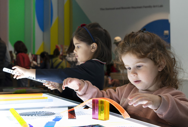 Photo: Martin Seck Image description: Two children build with transparent shapes and lines at a glowing light table