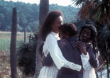 Daughters of the Dust. 1991. USA. Directed by Julie Dash. The Museum of Modern Art, New York. Film Study Collection Image Description: Three Black women embrace with pensive, furrowed expressions. They stand in a tropical field, surrounded by palm trees and tall grasses. A lush forest stands in the hazy background.