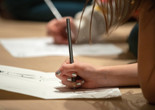 Photo: Manuel Martagon Image description: A close-up of a child’s hand holding a pencil and drawing on paper while sitting on the ground